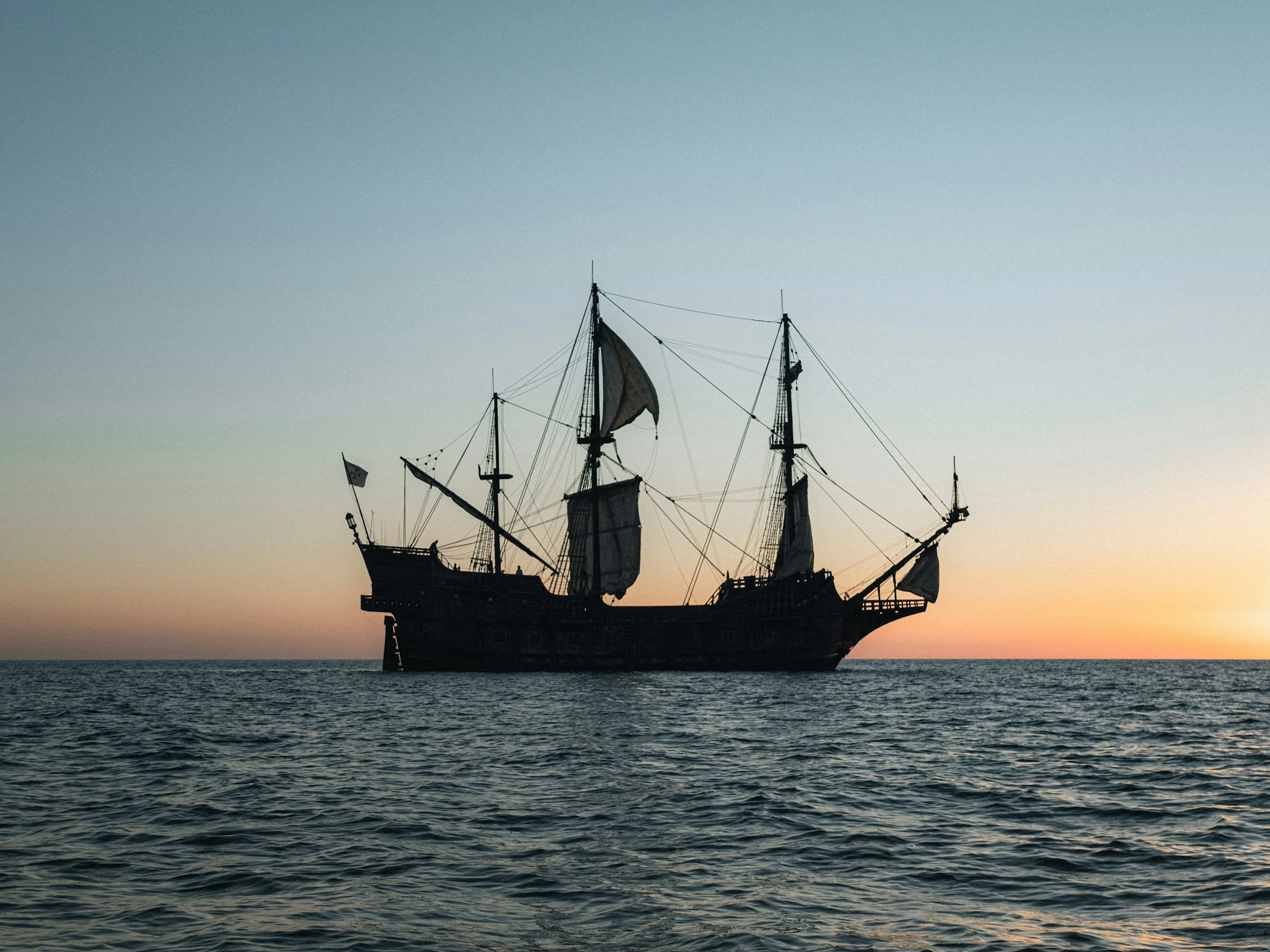 Tall ship sailing the open ocean at sunset